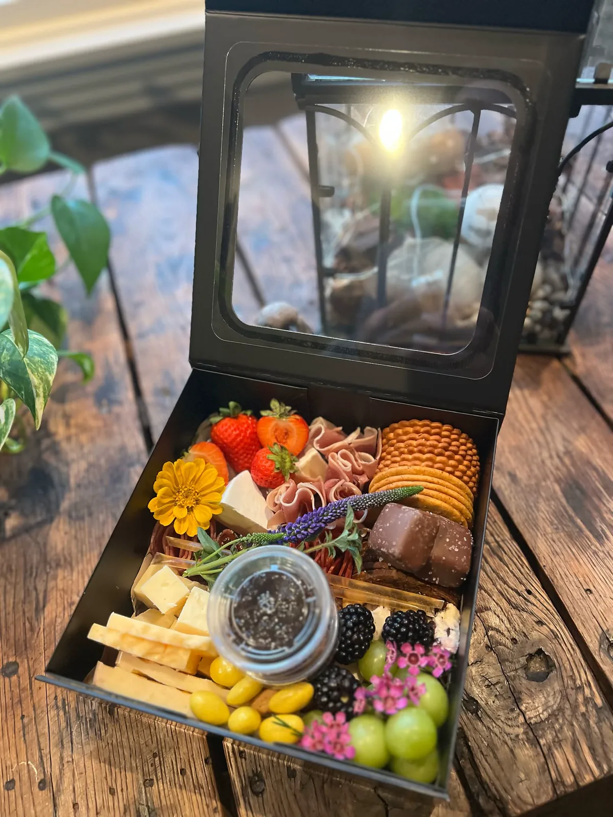 Open A La Cart charcuterie box with meats, cheeses, crackers, fruit, and flowers