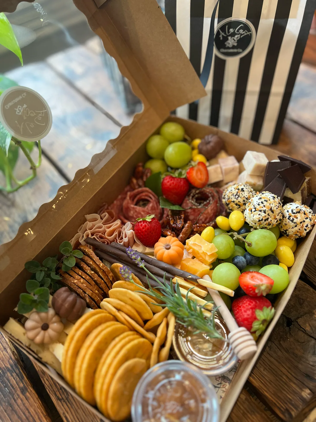 Open custom charcuterie box with meats, cheeses, fruit, crackers, and garnish