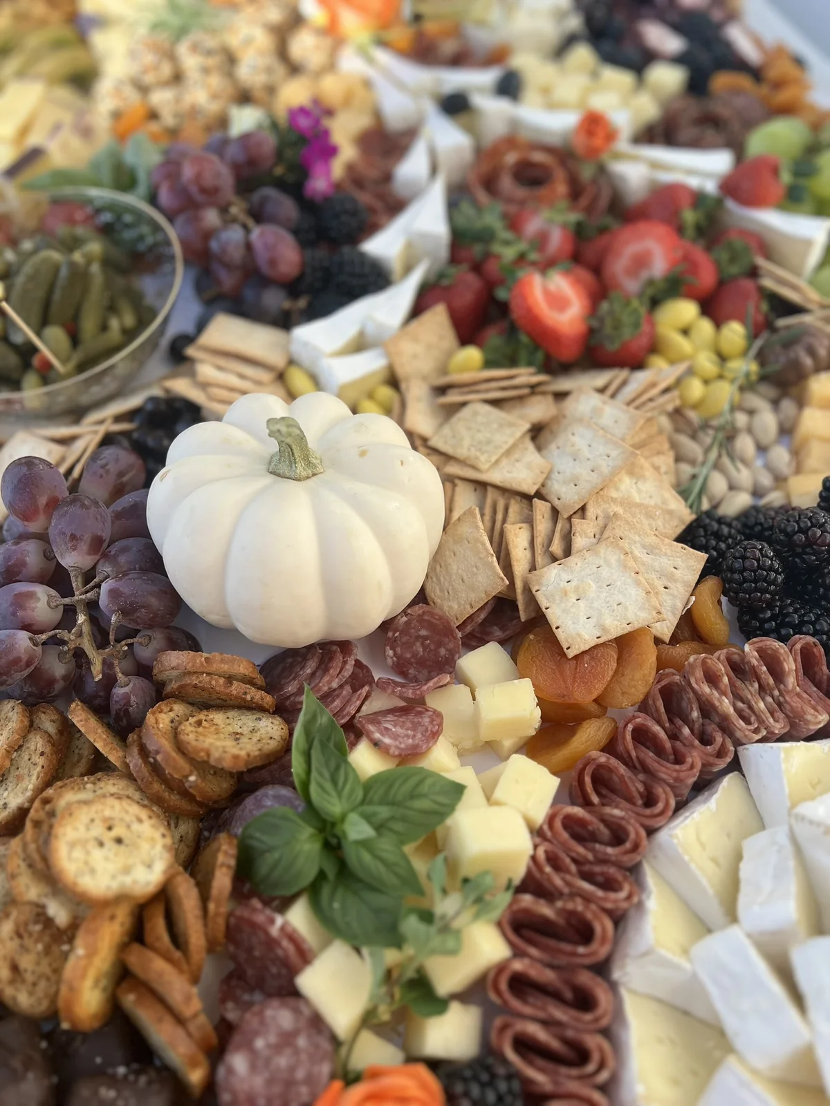 White pumpkin surrounded by grapes, crackers, cheeses, and charcuterie in an autumn grazing spread