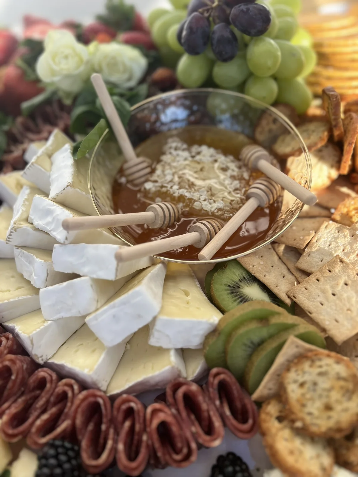 Brie, honeycomb, honey dippers, kiwi, and crackers on an October grazing table