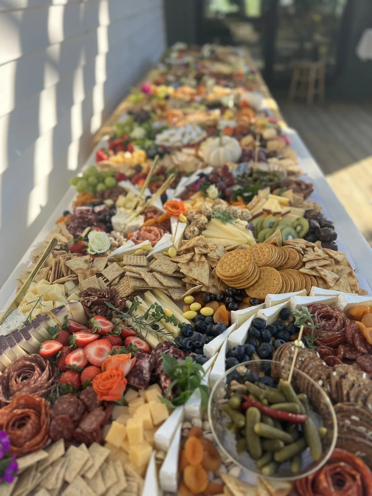 October grazing table viewed along its full length with charcuterie, cheeses, fruit, and flowers