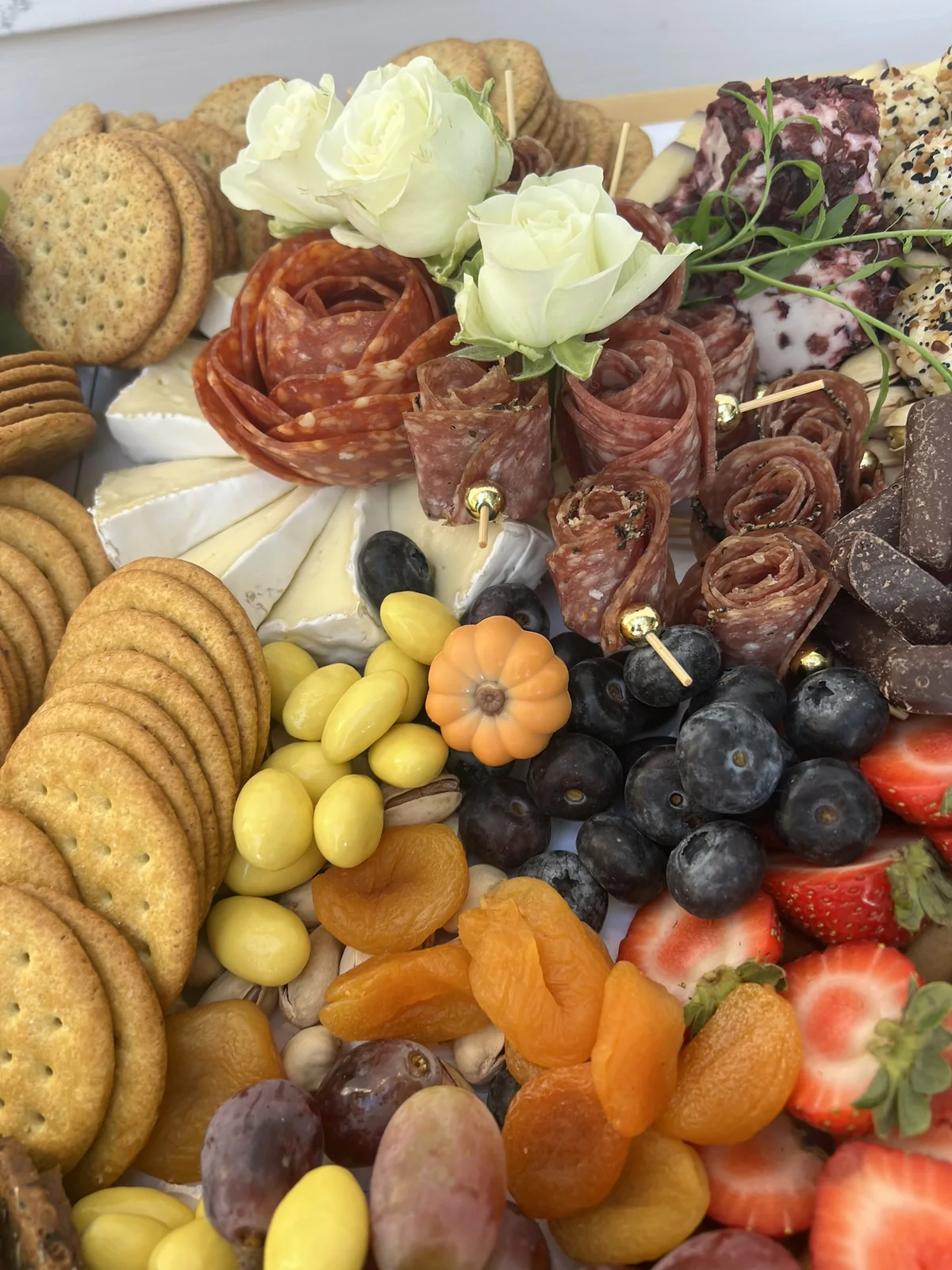 White roses, salami, crackers, blueberries, and dried apricots on an October grazing table