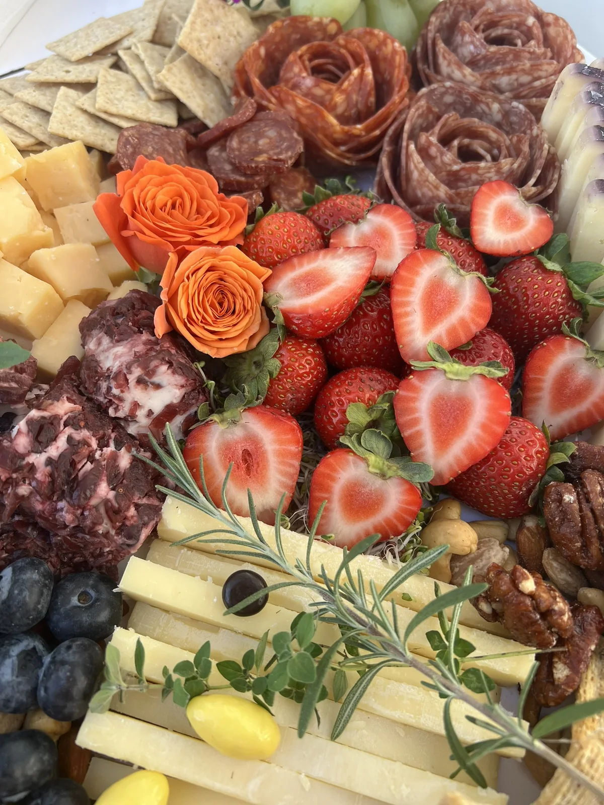 Strawberries, salami roses, orange flowers, and cheeses on an October grazing table